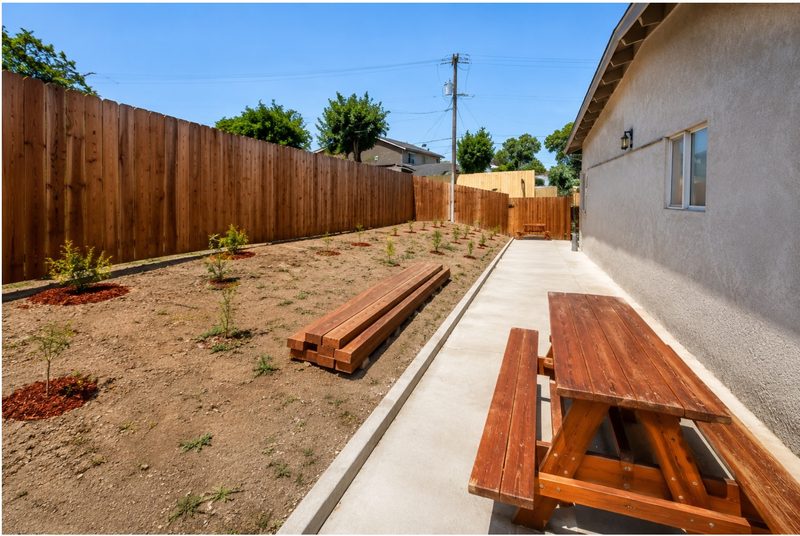 Fenced back yard with picnic tables along a concrete walkway